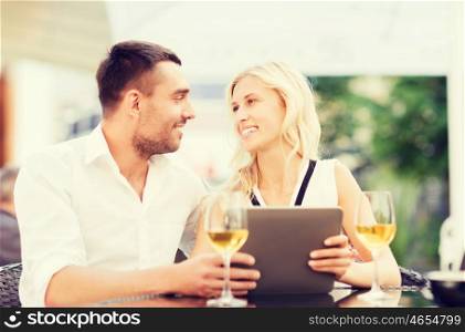 love, dating, people, technology and holidays concept - happy couple with tablet pc computer and glasses of wine at restaurant lounge or terrace