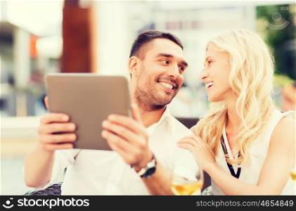 love, dating, people, technology and holidays concept - happy couple with tablet pc computer talking at restaurant lounge or terrace