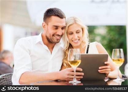 love, dating, people, technology and holidays concept - happy couple with tablet pc computer and glasses of wine at restaurant lounge or terrace