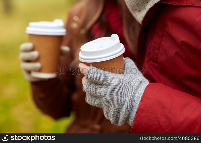 love, drinks and people concept - close up of couple hands with coffee cups in autumn park