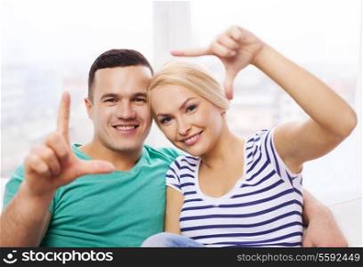 love, family and happiness concept - smiling happy couple making frame gesture at home