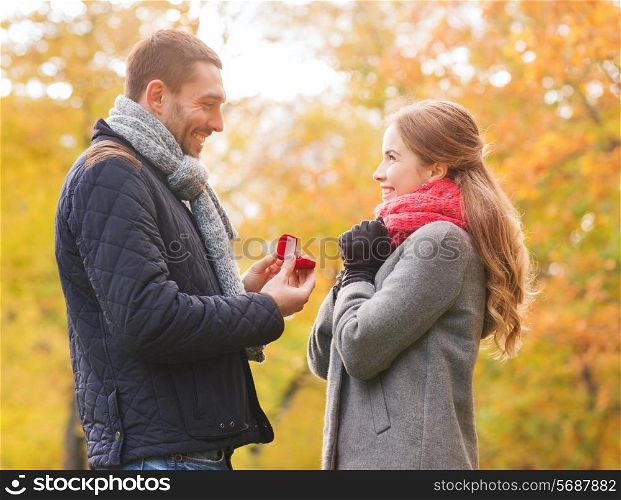 love, family, autumn and people concept - smiling couple with engagement ring in small red gift box outdoors