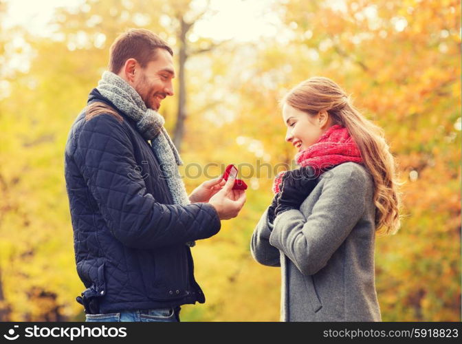 love, family, autumn and people concept - smiling couple with engagement ring in small red gift box outdoors