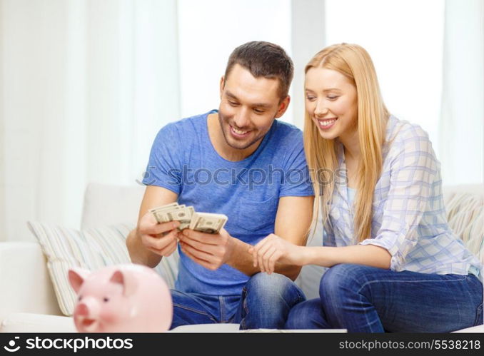 love, family, finance, money and happiness concpet - smiling couple counting money with piggybank ot table at home