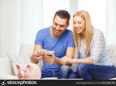 love, family, finance, money and happiness concpet - smiling couple counting money with piggybank ot table at home