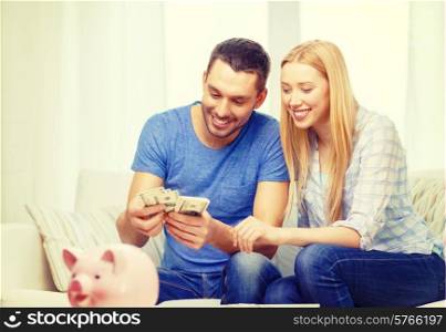 love, family, finance, money and happiness concpet - smiling couple counting money with piggybank ot table at home