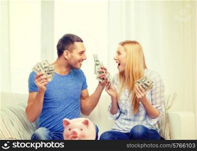love, family, finance, money and happiness concpet - smiling couple with money and piggybank ot table at home
