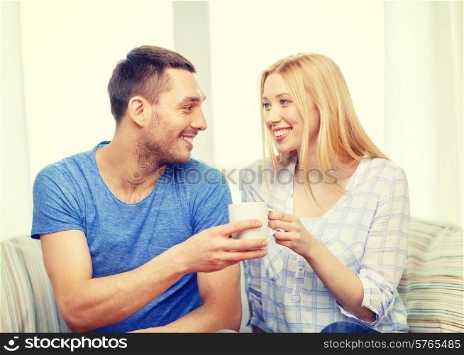 love, family, healthy food and happiness concept - smiling man giving cup of tea or coffee to wife or girlfriend at home