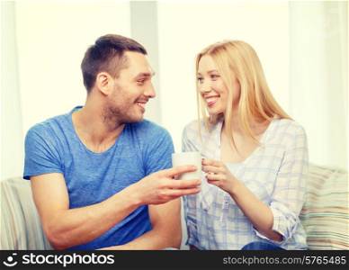 love, family, healthy food and happiness concept - smiling man giving cup of tea or coffee to wife or girlfriend at home