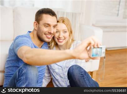 love, family, technology and happiness concept - smiling couple taking self portrait picture with digital camera at home