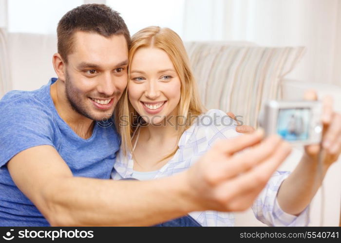 love, family, technology and happiness concept - smiling couple taking self portrait picture with digital camera at home