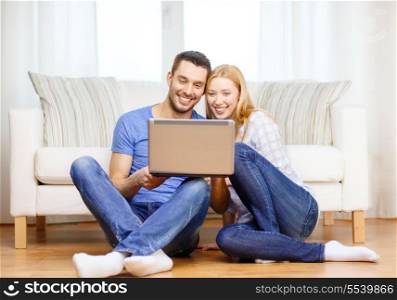 love, family, technology, internet and happiness concept - smiling happy couple with laptop computer sitting on the floor at home