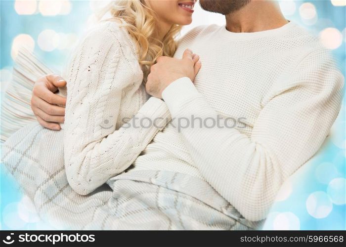 love, family, winter and happiness concept - close up of happy couple cuddling under paid at home over blue lights background