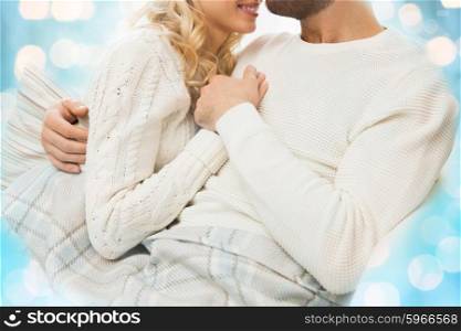 love, family, winter and happiness concept - close up of happy couple cuddling under paid at home over blue lights background