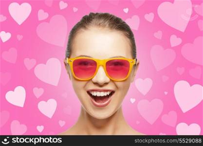 love, happiness and valentines day concept - amazed teen girl in pink sunglasses on background with hearts