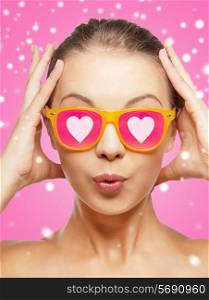 love, happiness, holidays, christmas and people concept - smiling teenage girl in sunglasses with hearts over pink background