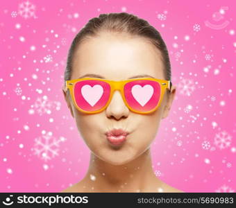 love, happiness, holidays, christmas and people concept - smiling teenage girl in sunglasses with hearts over pink background