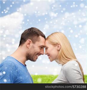 love, happiness, people and family concept - smiling couple looking at each other over blue sky, snow and grass background