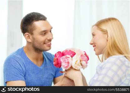 love, holiday, celebration and family concept - smiling man giving girfriens flowers at home