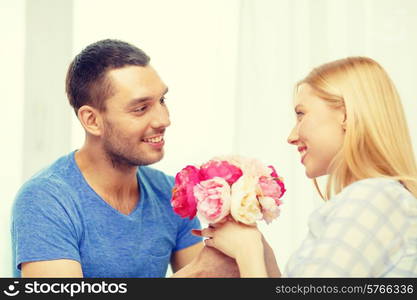 love, holiday, celebration and family concept - smiling man giving girfriens flowers at home