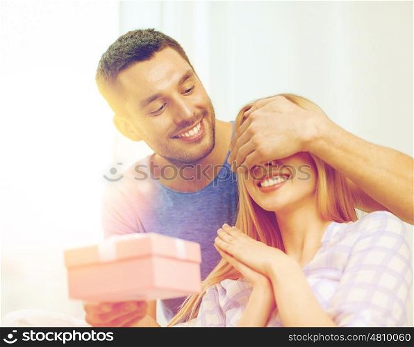 love, holiday, celebration and family concept - smiling man surprises his girlfriend with present at home