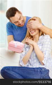 love, holiday, celebration and family concept - smiling man surprises his girlfriend with present at home