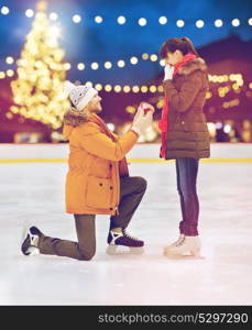 love, holidays and relationships concept - happy couple with engagement ring at outdoor skating rink over christmas lights background. couple with engagement ring at xmas skating rink