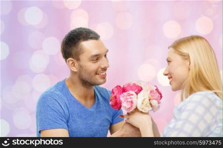 love, holidays, valentines day and relations concept - smiling man giving woman flowers at home over pink lights background