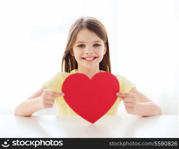 love, home, happiness and people concept - smiling little girl with red heart at home