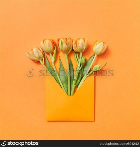 Love letter yellow freshly picked flowers in a handmade envelope on an orange background with lace for text. Flat lay.. Fresh spring tulips as a gift in a craft envelope on an orange background.