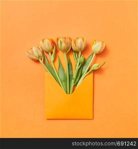 Love letter yellow freshly picked flowers in a handmade envelope on an orange background with lace for text. Flat lay.. Fresh spring tulips as a gift in a craft envelope on an orange background.