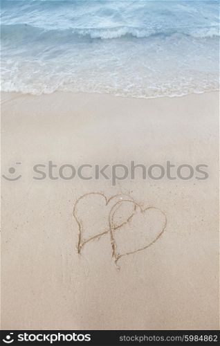 Love on beach concept. Love on beach concept - two hearts on a beach sand with coming wave