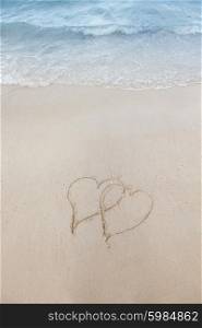Love on beach concept. Love on beach concept - two hearts on a beach sand with coming wave