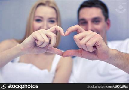 love, people and happiness concept - close up of smiling couple in bed making heart shape gesture
