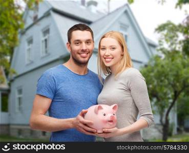 love, people, real estate, home and family concept - smiling couple holding piggy bank over house background
