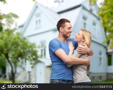 love, people, real estate, home and family concept - smiling couple hugging over house background