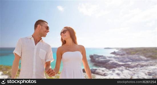 love, people, travel and relations concept - happy couple wearing sunglasses holding hands over summer beach and sea background