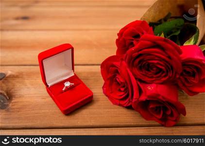 love, proposal, valentines day and holidays concept - close up of gift box with diamond engagement ring and red roses on wood