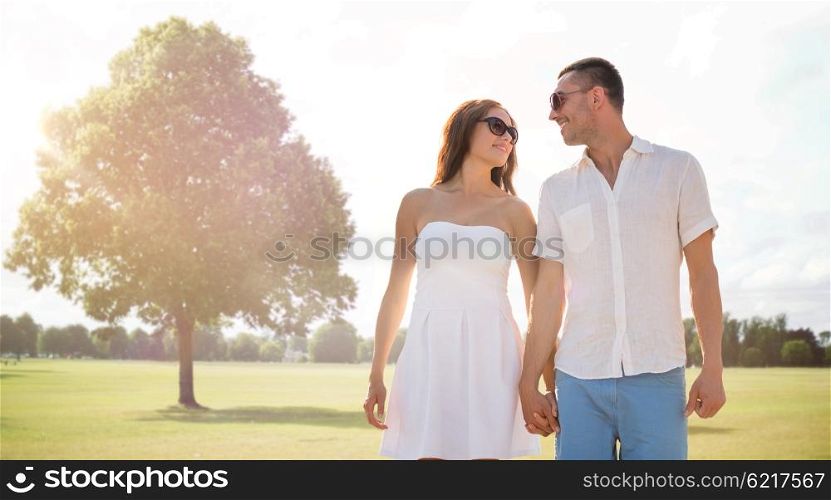 love, relations, holidays, dating and people concept - happy couple wearing sunglasses walking over summer park background