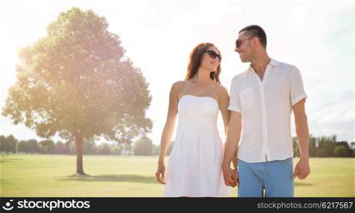 love, relations, holidays, dating and people concept - happy couple wearing sunglasses walking over summer park background