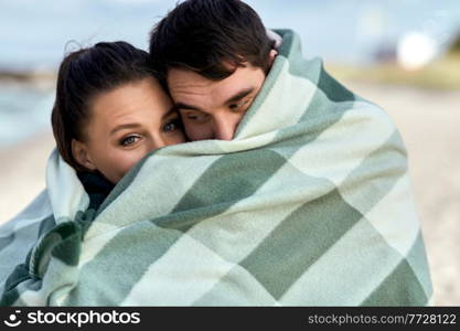 love, relationship and people concept - happy smiling couple in warm blanket on autumn beach. happy couple in warm blanket on autumn beach