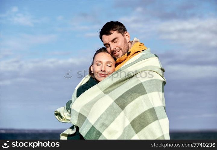 love, relationship and people concept - happy smiling couple in warm blanket on autumn beach. happy couple in warm blanket on autumn beach