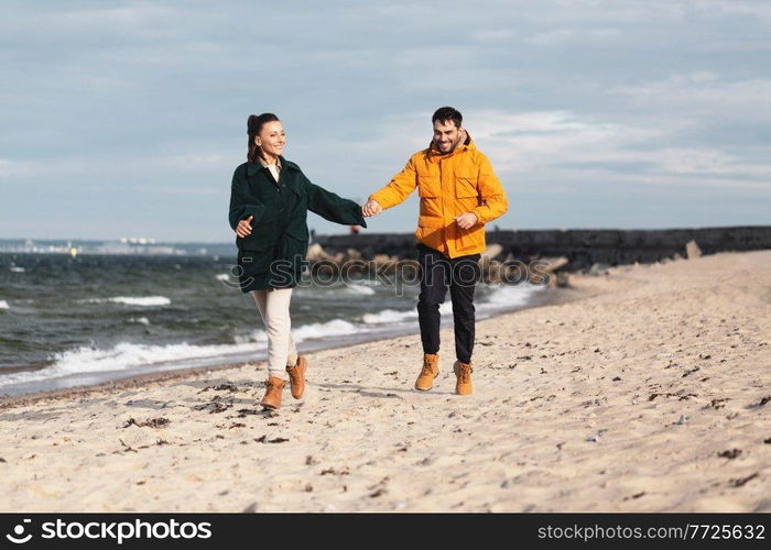 love, relationship and people concept - happy smiling couple running along autumn beach and holding hands. couple running along autumn beach