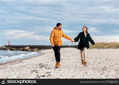 love, relationship and people concept - happy smiling couple running along autumn beach and holding hands. couple running along autumn beach