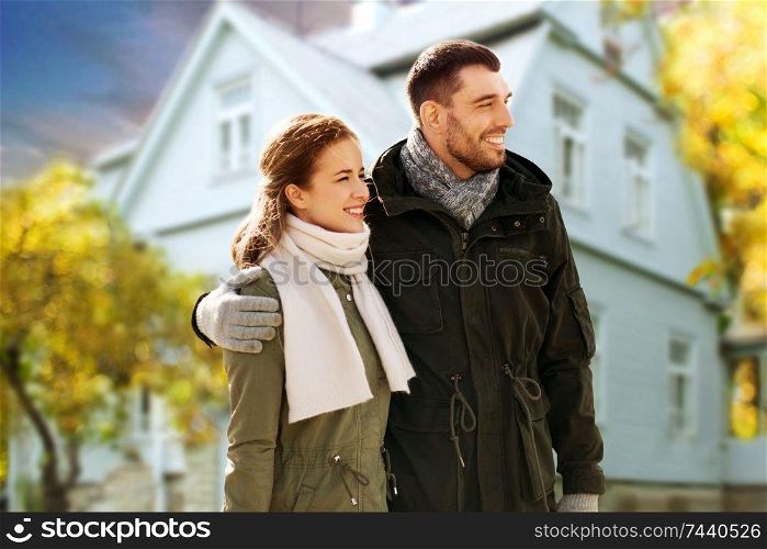 love, relationship and people concept - smiling couple hugging over house in autumn background. smiling couple hugging over house in autumn