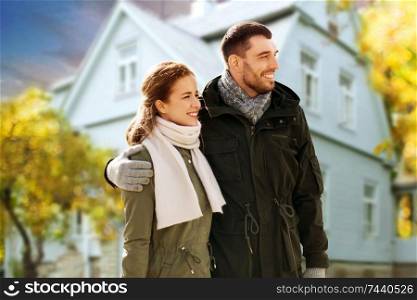 love, relationship and people concept - smiling couple hugging over house in autumn background. smiling couple hugging over house in autumn