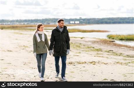 love, relationship and people concept - smiling couple walking along autumn beach and holding hands. couple walking along autumn beach