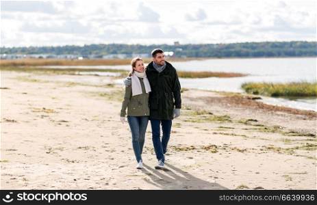 love, relationship and people concept - smiling couple walking along autumn beach and holding hands. couple walking along autumn beach