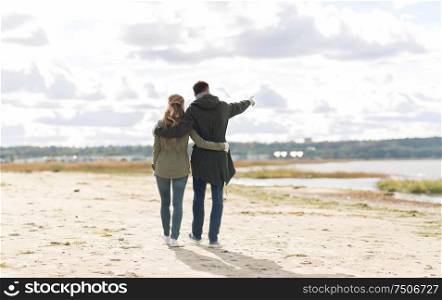 love, relationship and people concept - smiling couple walking along autumn beach and hugging. couple walking along autumn beach and hugging