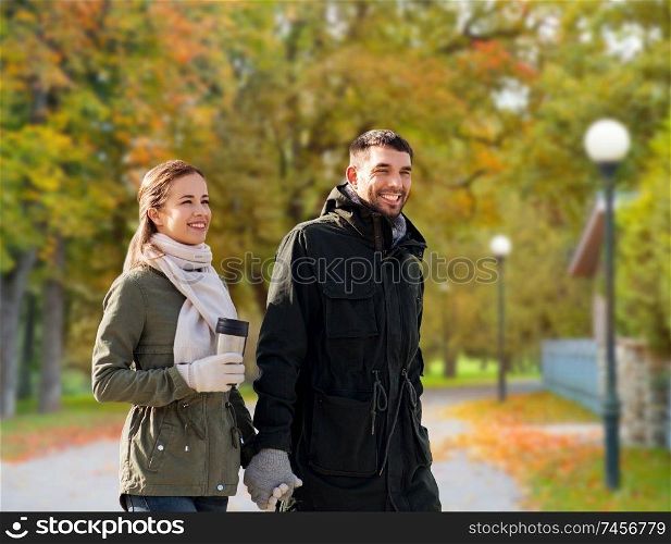 love, relationship and season concept - smiling couple with tumbler walking over autumn park background. couple with tumbler walking along autumn park
